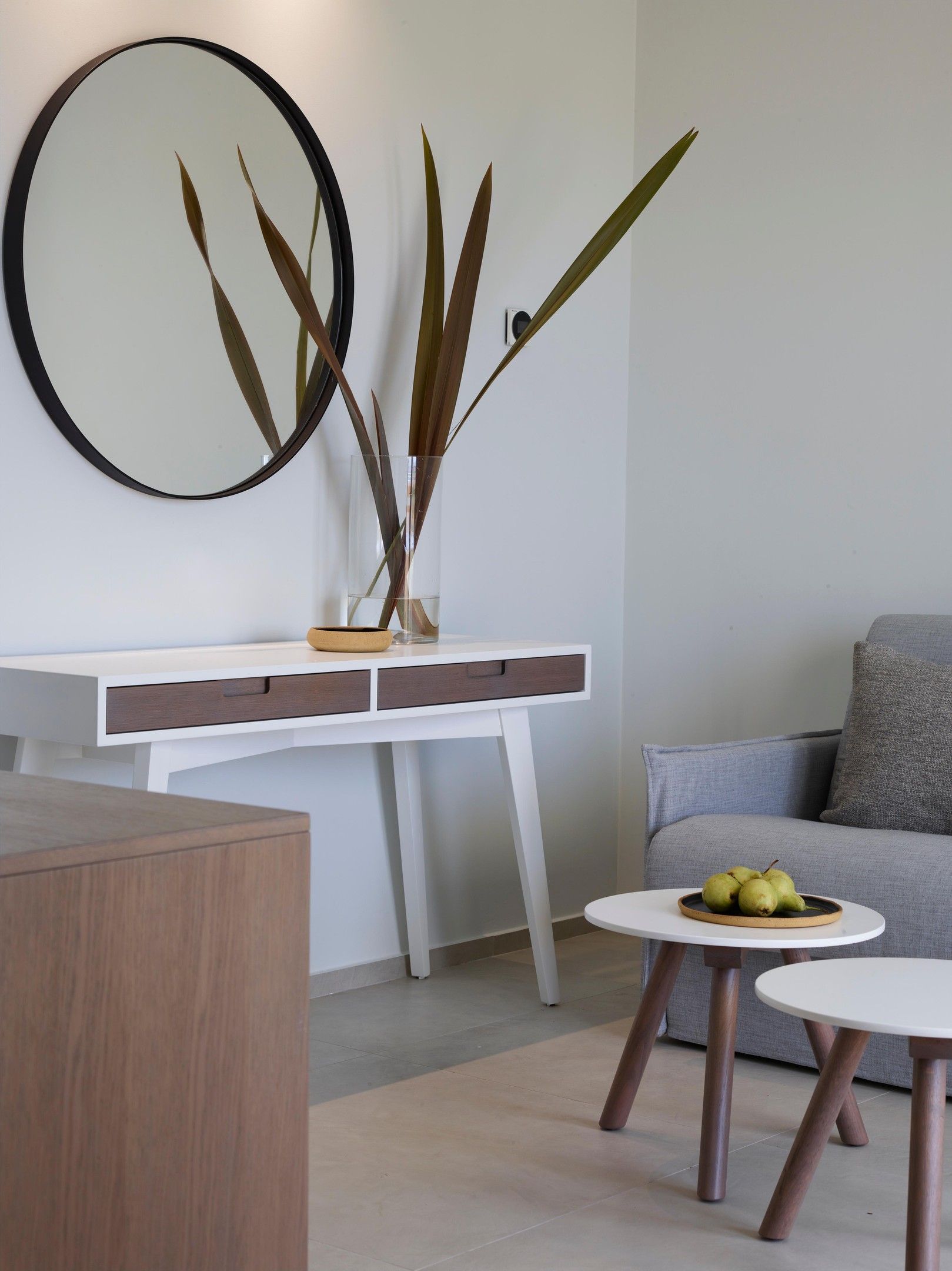A modern living room with a white console table, a round mirror, and a grey sofa.