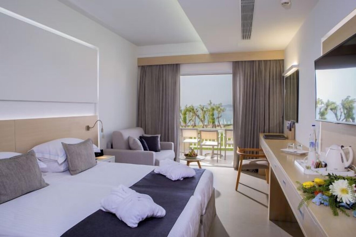 A hotel room with a bed, a desk, a chair, and a balcony with a view.