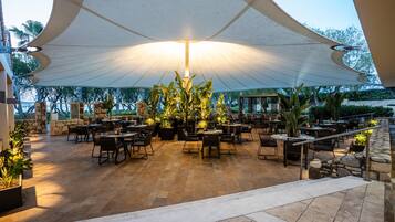 An outdoor patio area with tables and chairs, a large canopy, and potted plants.