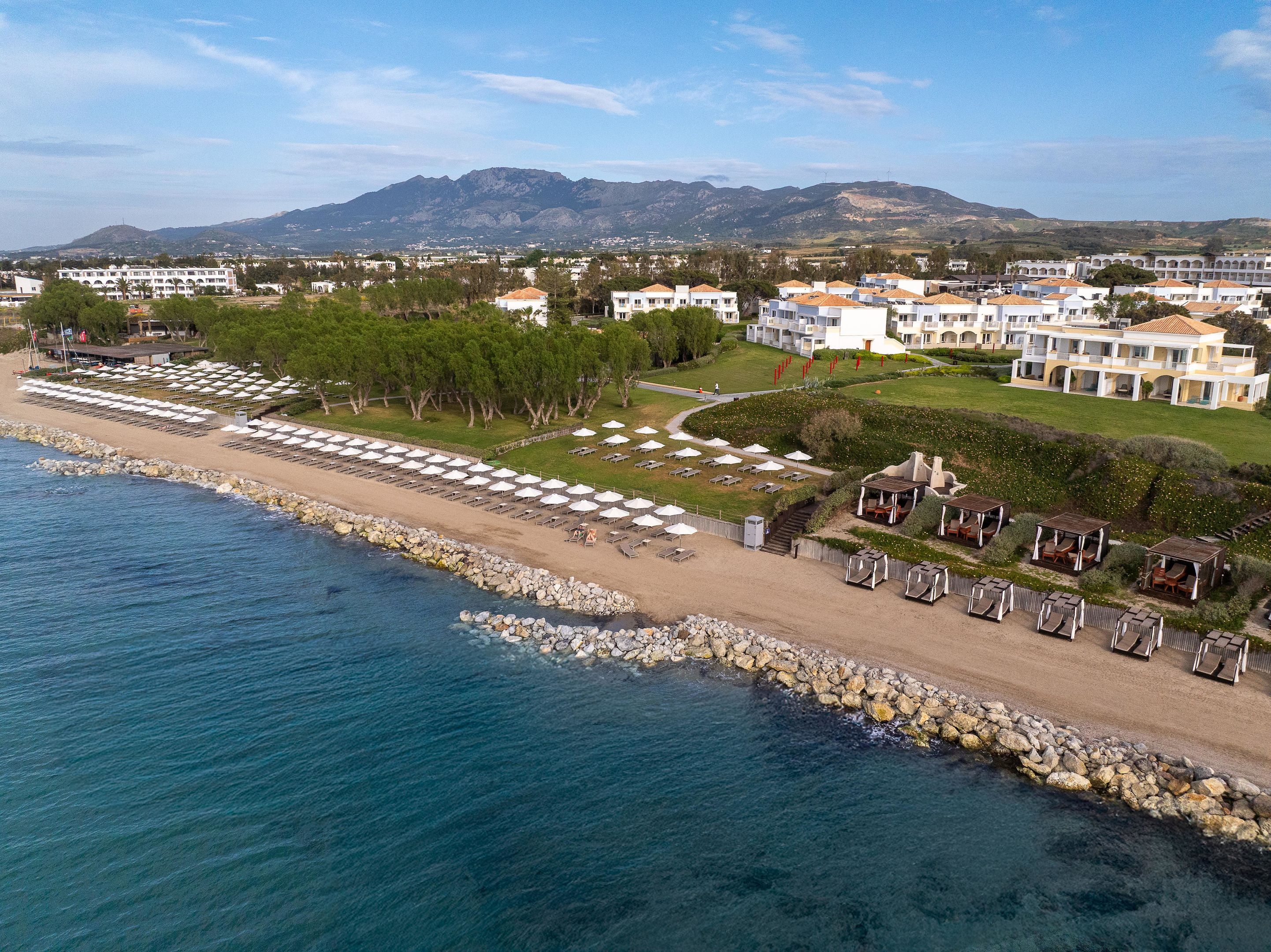 Un resort costero con villas frente a la playa, una playa de arena y un litoral rocoso.
