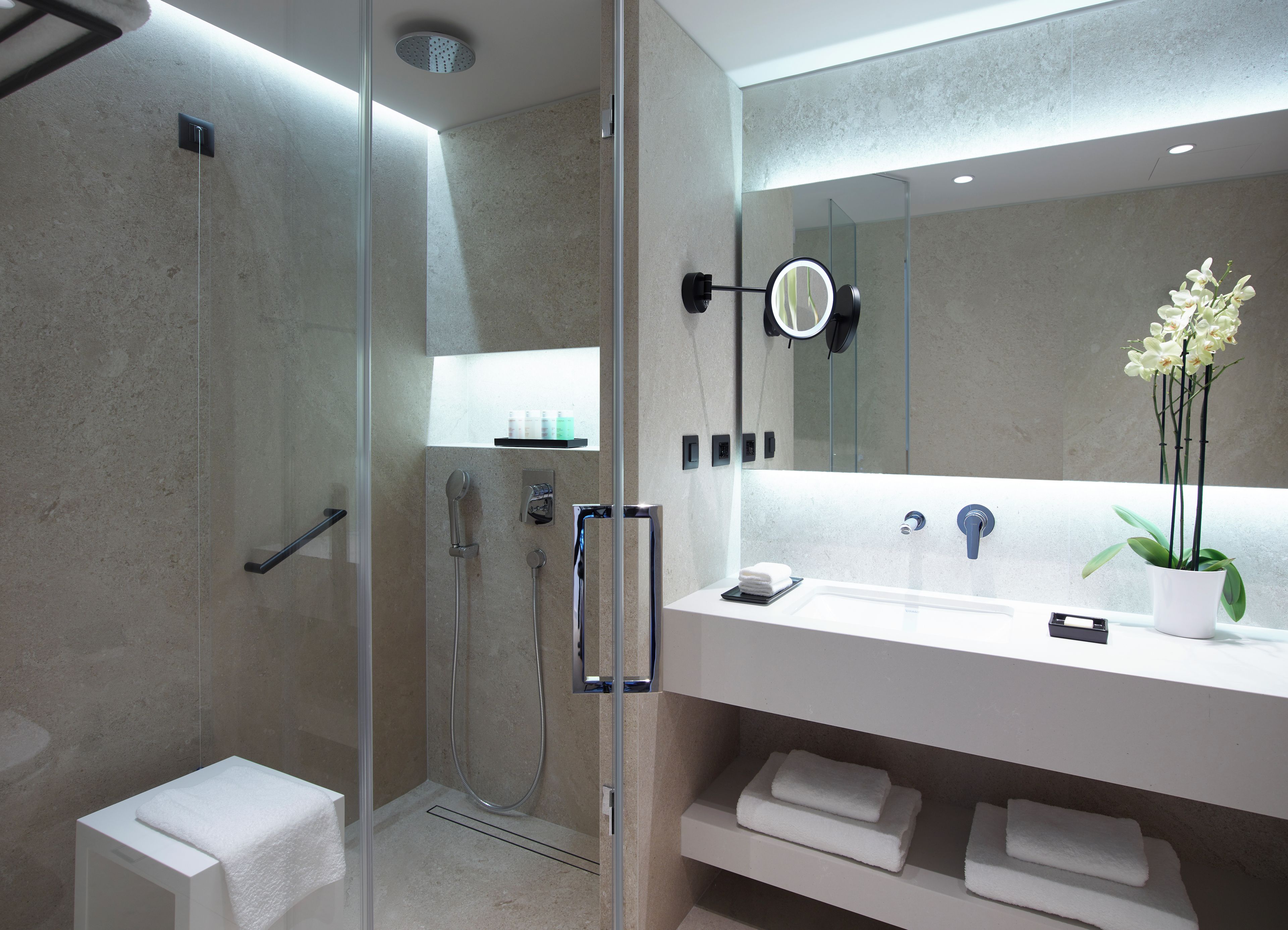 A modern bathroom with a glass-enclosed shower, a white sink with a mirror, and a potted orchid.