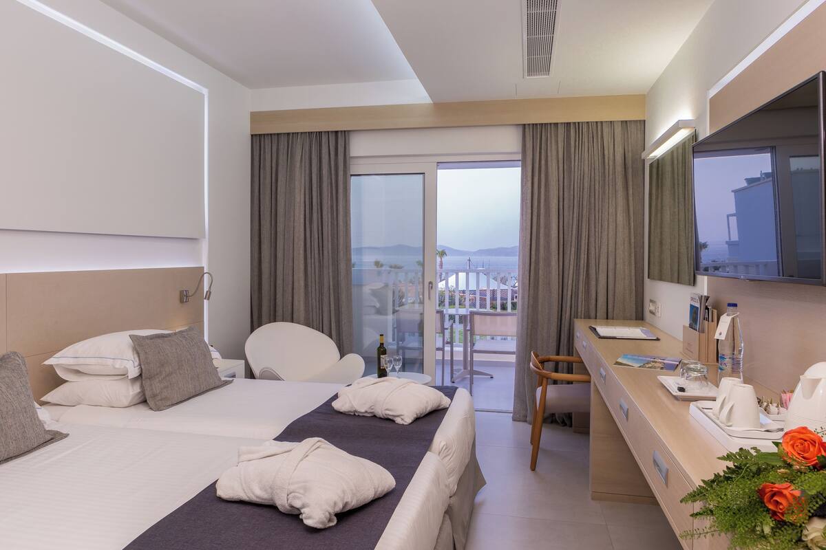 A hotel room with a bed, a desk, a chair, a bathroom, and a balcony with a view.