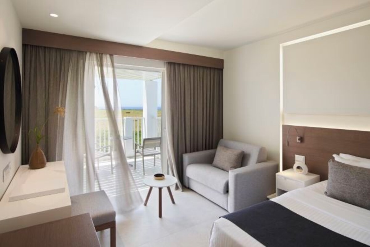 A hotel room with a bed, a sofa, a small table, a nightstand, and a view of the outdoors.