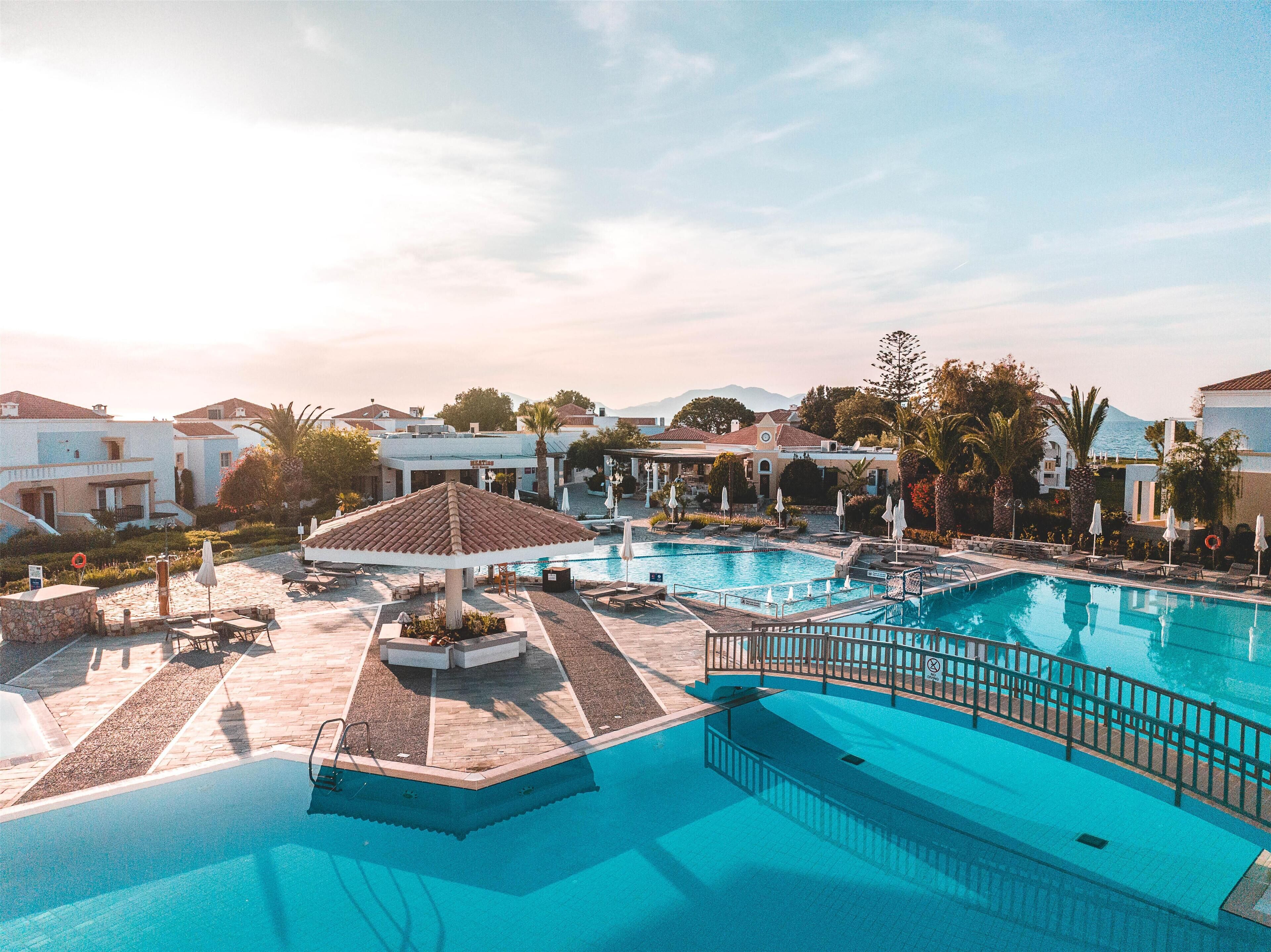 Área de piscina com espreguiçadeiras e guarda-sóis, cercada por edifícios e palmeiras.