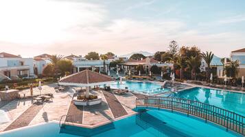 Área de piscina com espreguiçadeiras e guarda-sóis, cercada por edifícios e palmeiras.