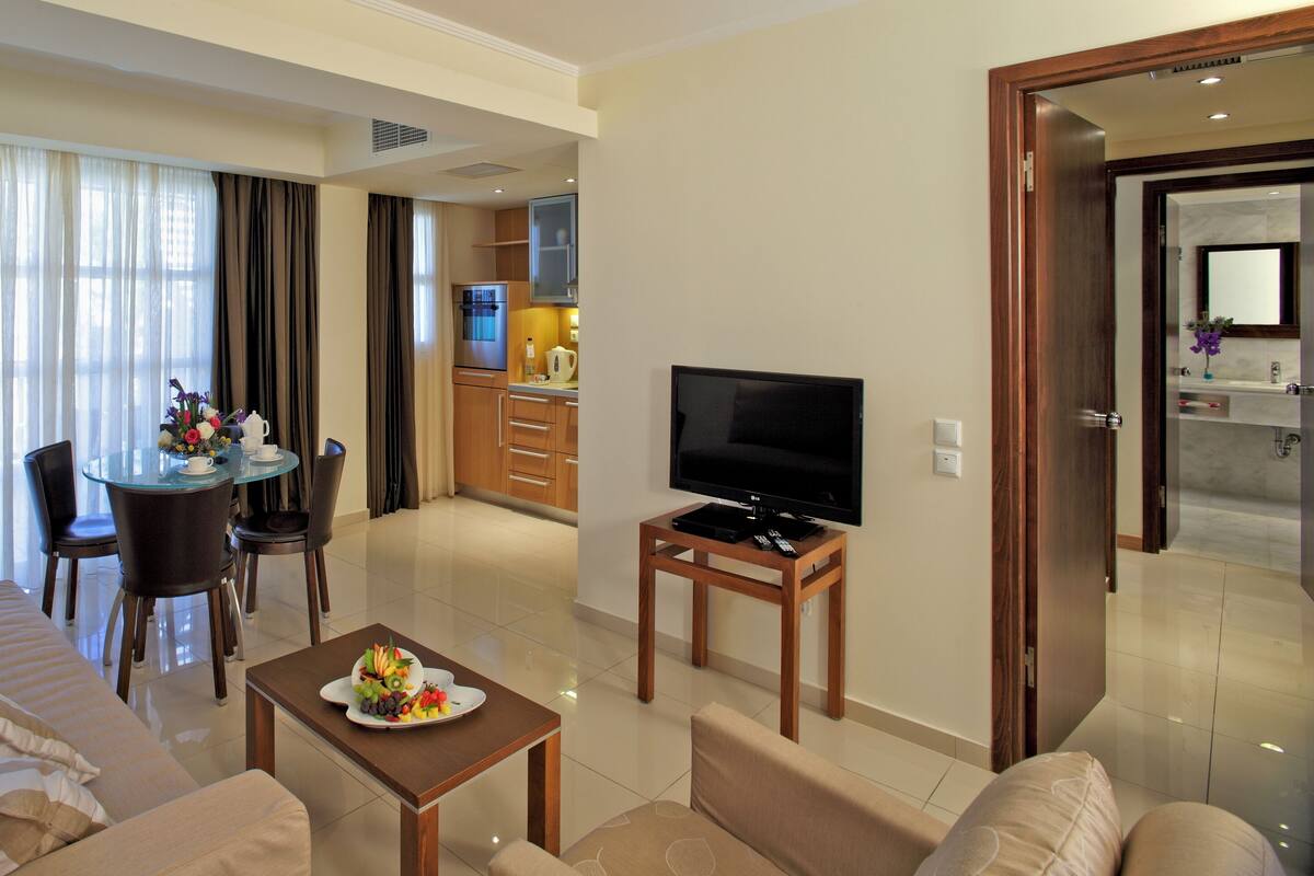 A modern hotel room with a living area, dining space, and a TV.