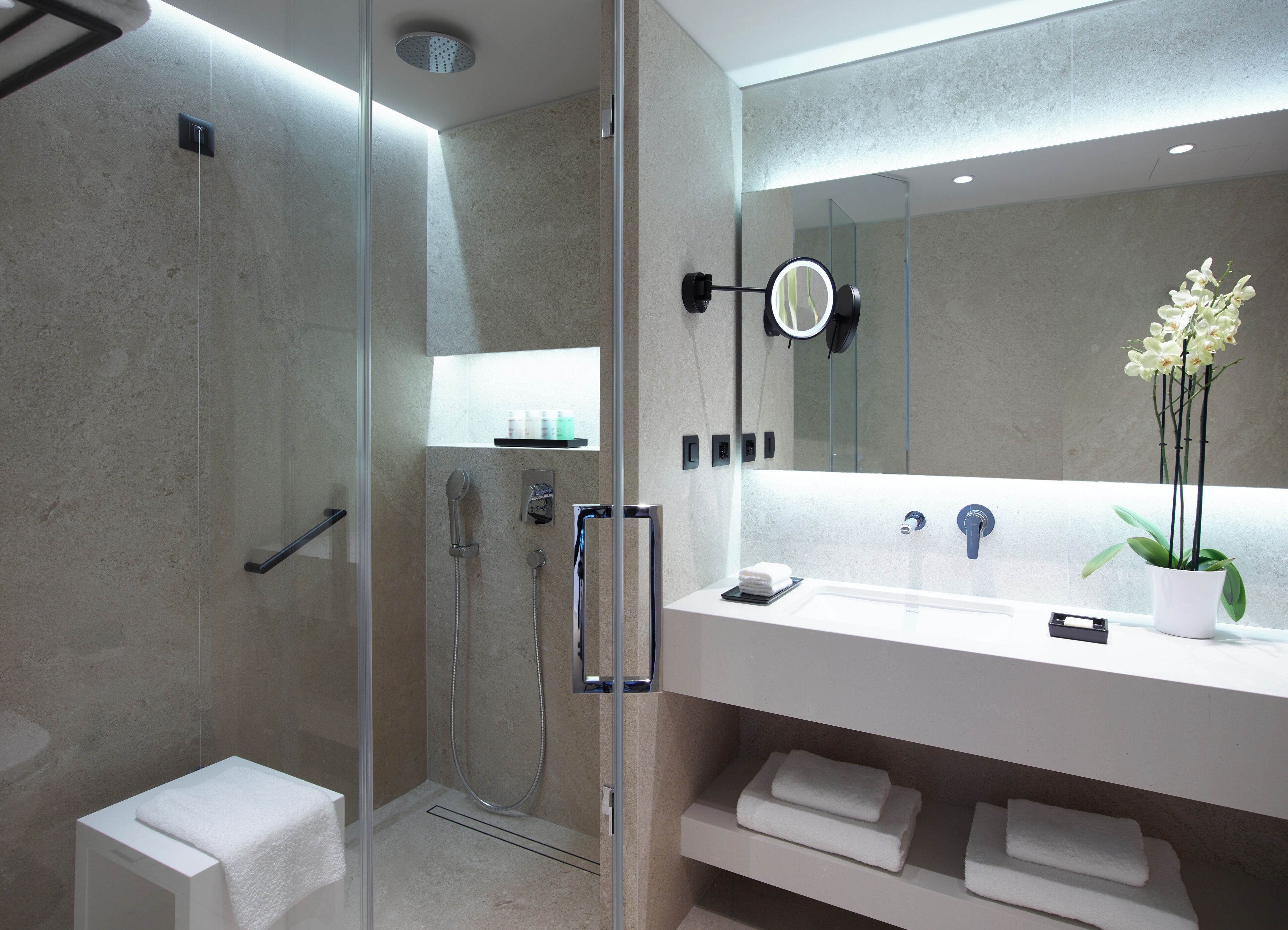 A modern bathroom with a glass-enclosed shower, a white sink with a mirror, and a potted orchid.