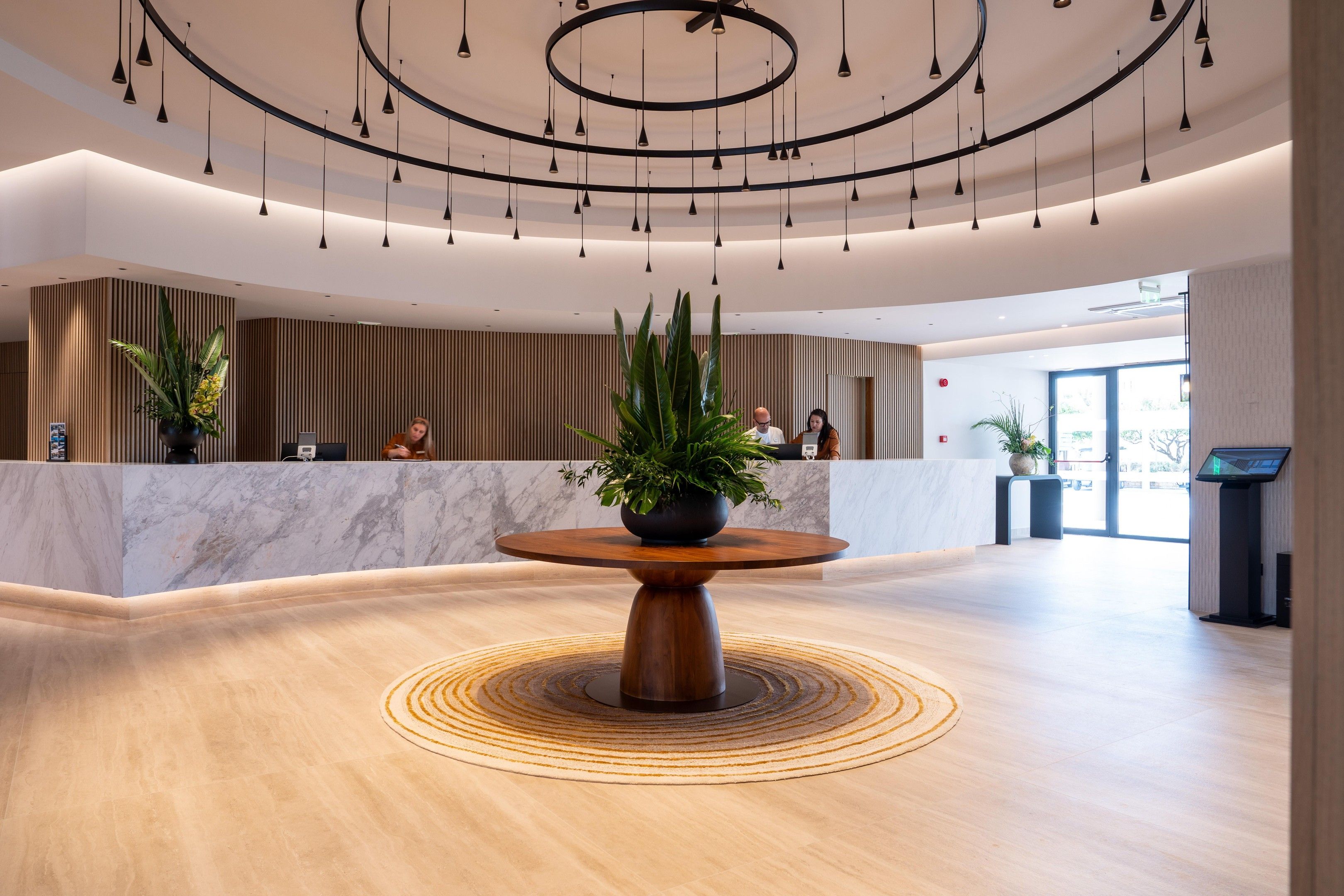 A modern reception area with a marble counter, a wooden reception desk, and a central table with a potted plant.