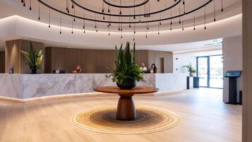 A modern reception area with a marble counter, a wooden reception desk, and a central table with a potted plant.