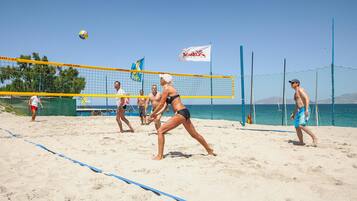 A beach volleyball game with players in action, a volleyball net, and a flag.