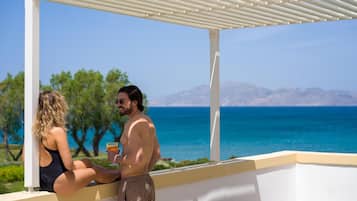 A man and a woman sitting on a balcony with a view of the sea and mountains.