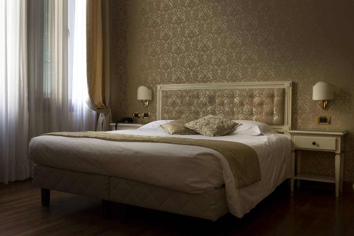 A large bed with a quilted headboard, two bedside tables with lamps, and a patterned wallpaper.