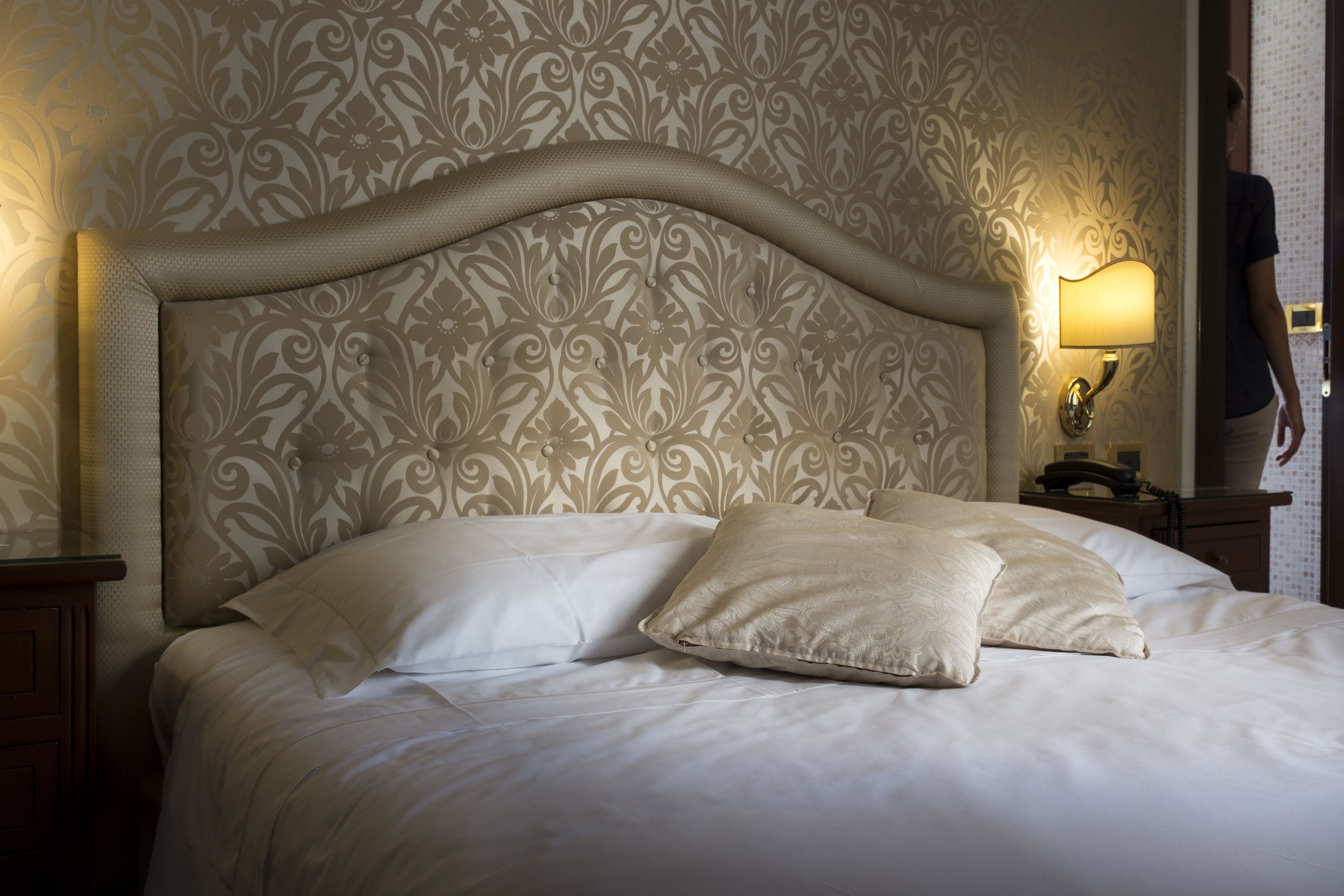 A neatly made bed with a decorative headboard, a bedside lamp, and a nightstand with a telephone.