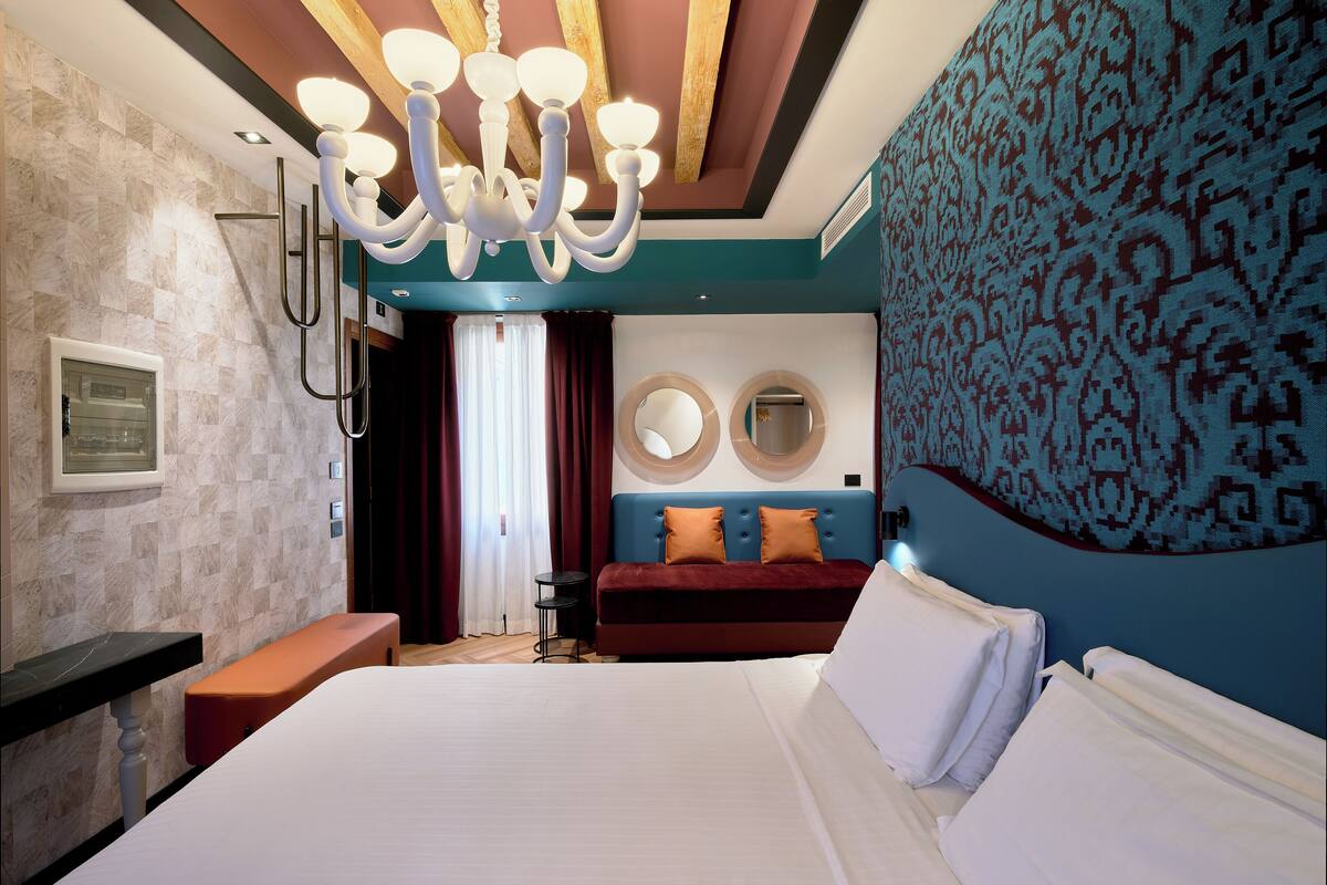 A modern hotel room with a large bed, a bench, a small table, and a chandelier.