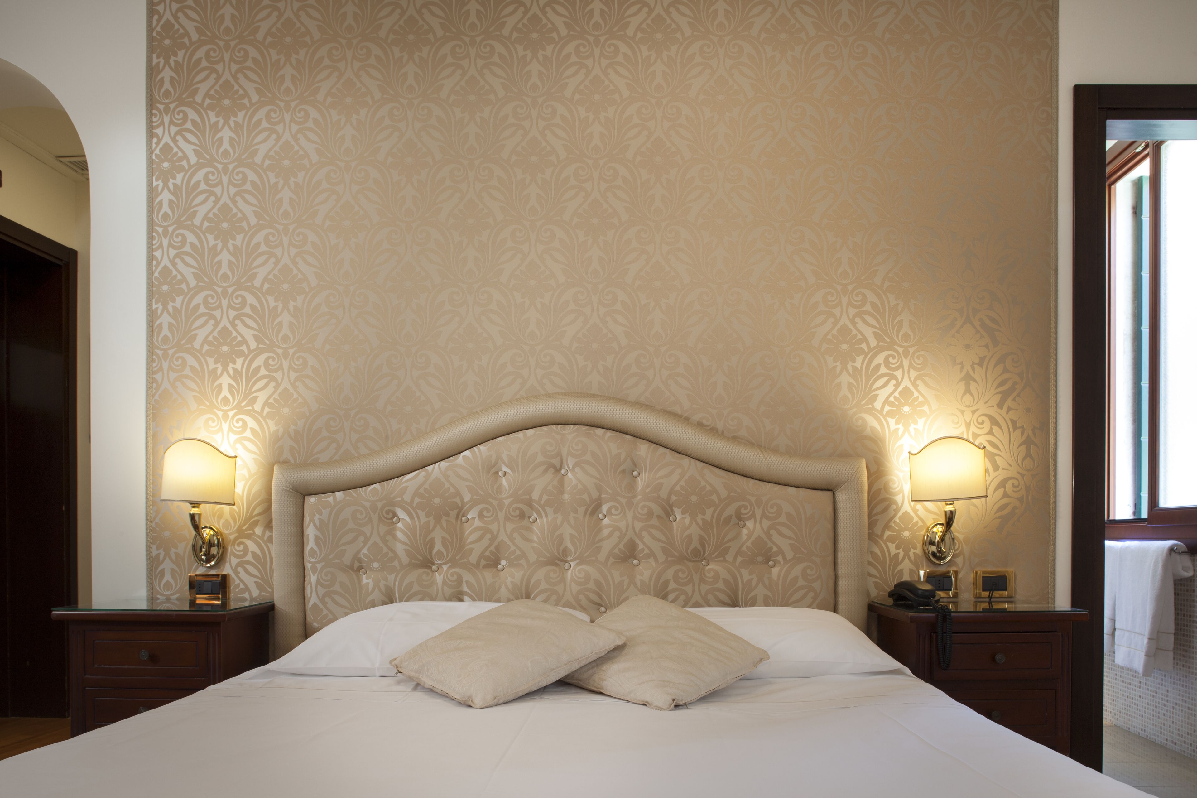 A hotel room with a large bed, two bedside lamps, and a patterned wallpaper.