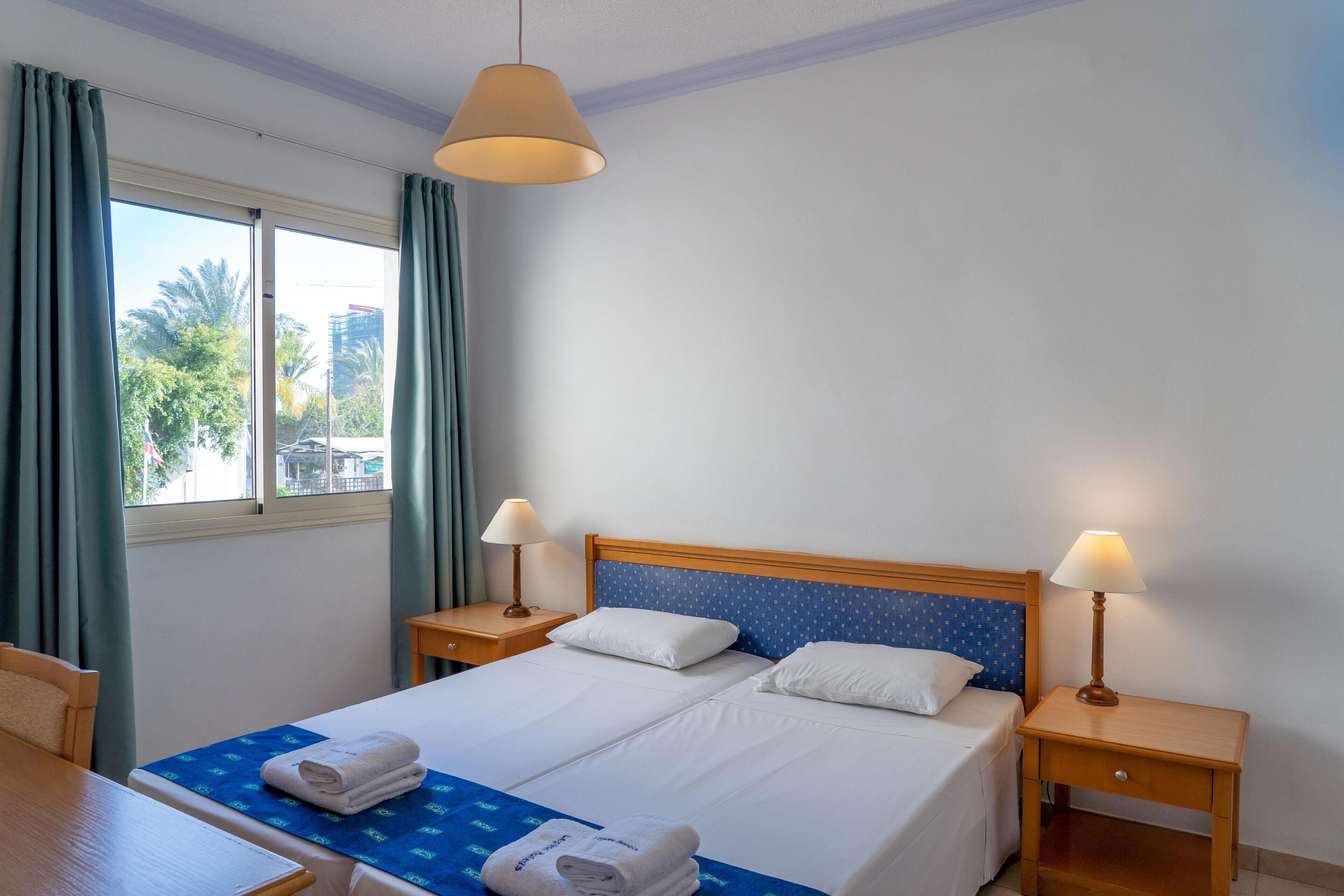 A hotel room with two beds, a wooden headboard, a window with curtains, and two bedside lamps.