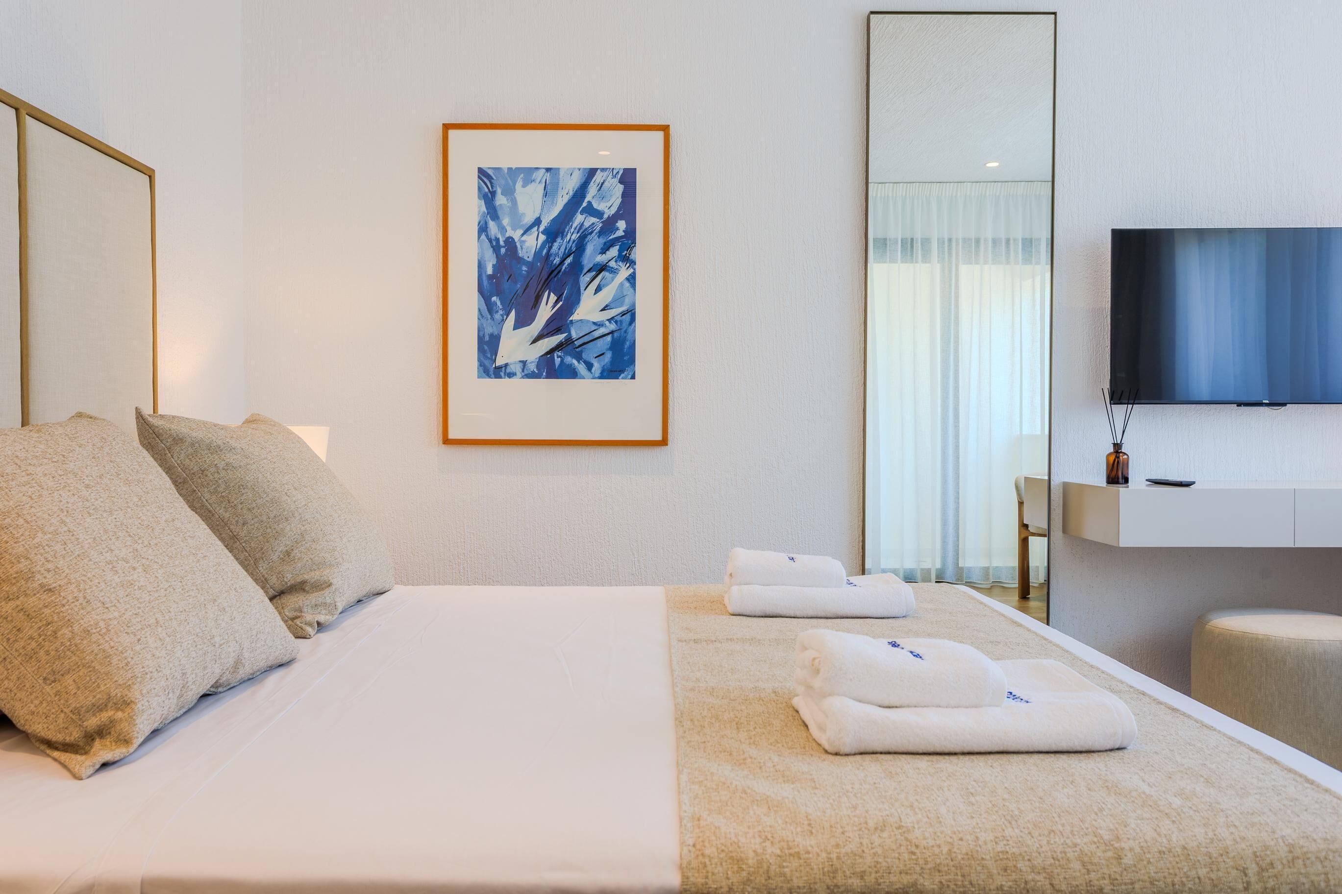 Habitación de hotel con cama, almohadas, una obra de arte enmarcada, televisor y mesita de noche con control remoto.
