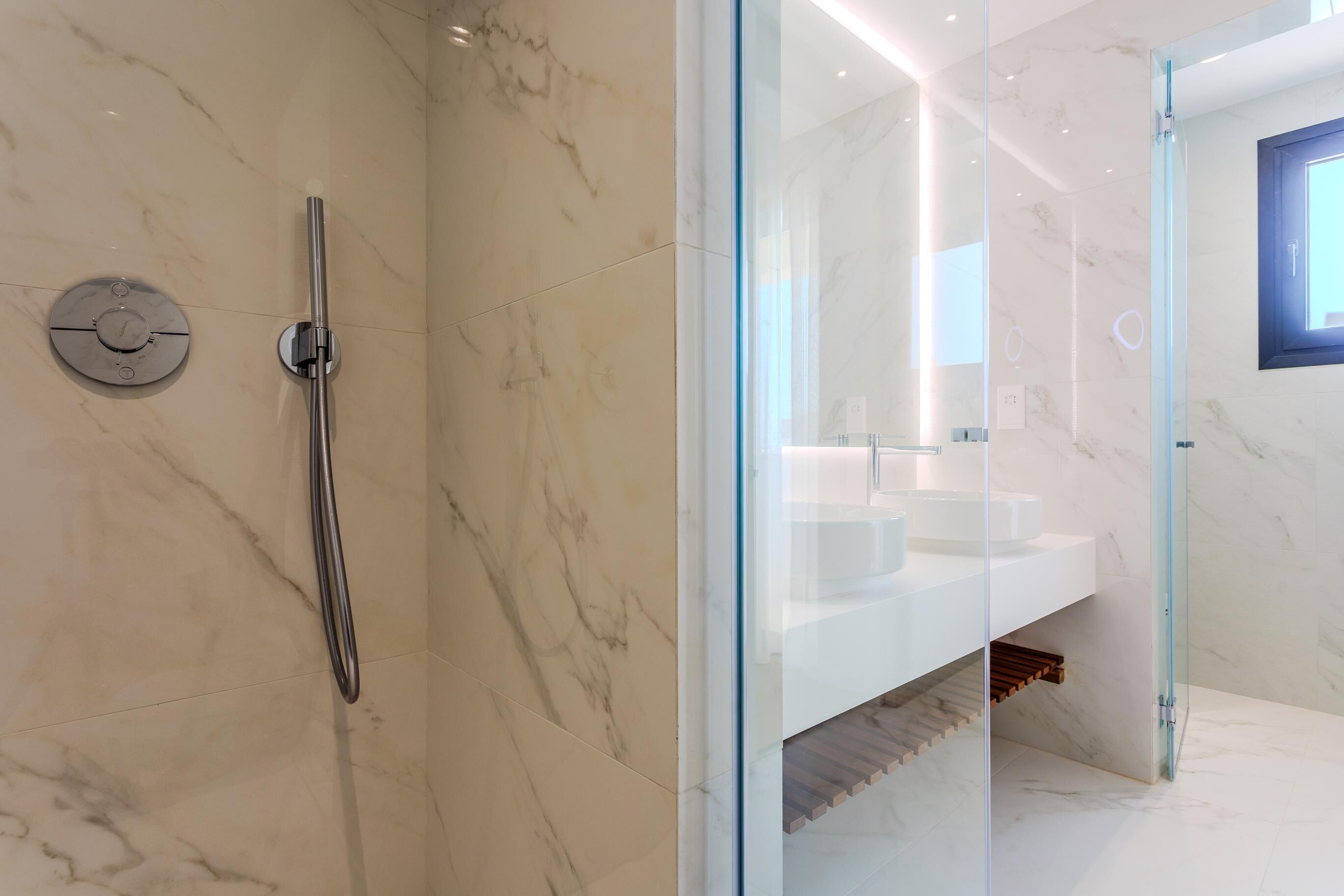 Une salle de bain moderne avec une douche à parois de verre, un lavabo blanc et un revêtement de sol en marbre.