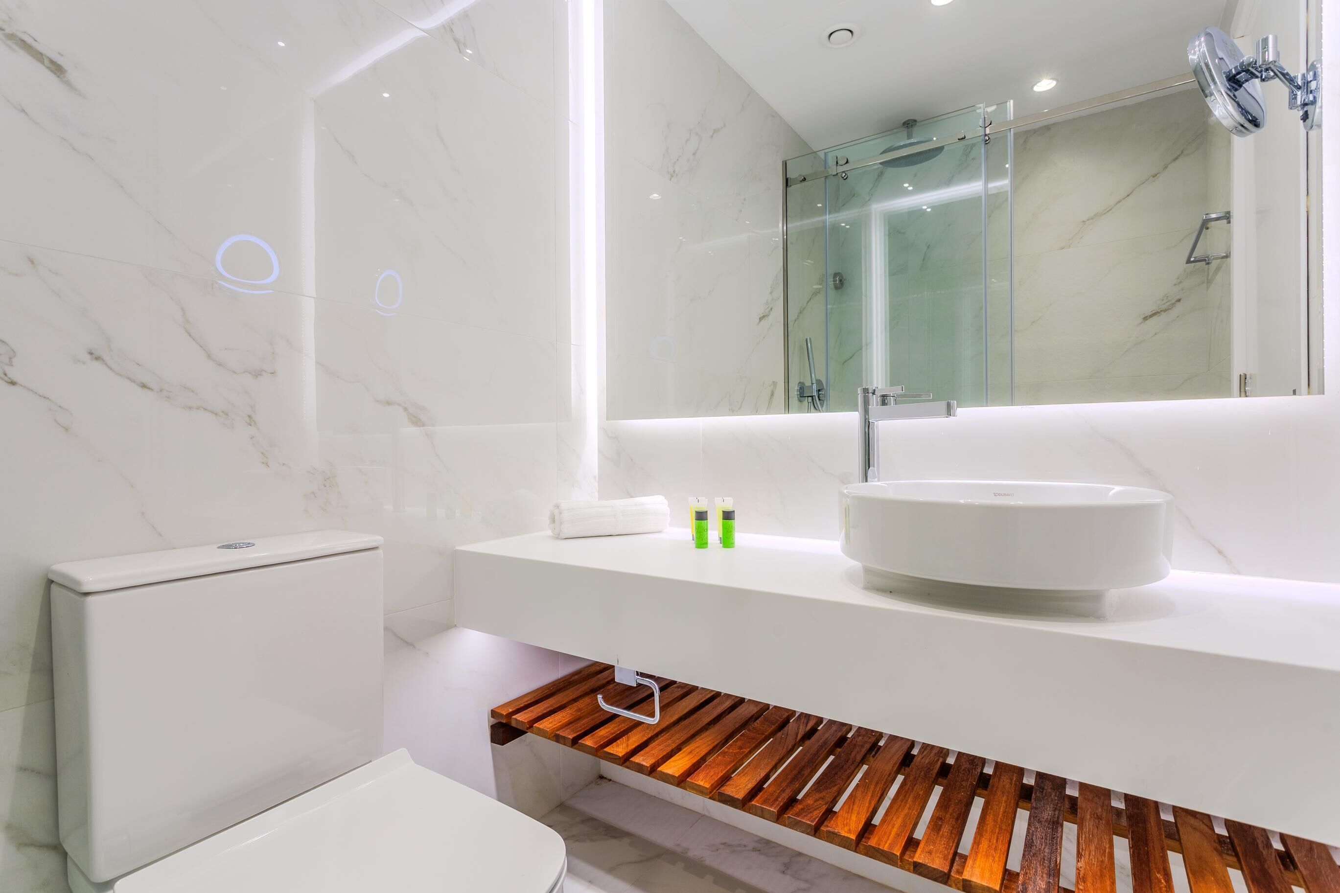 A modern bathroom with a white sink, marble walls, and a wooden vanity.