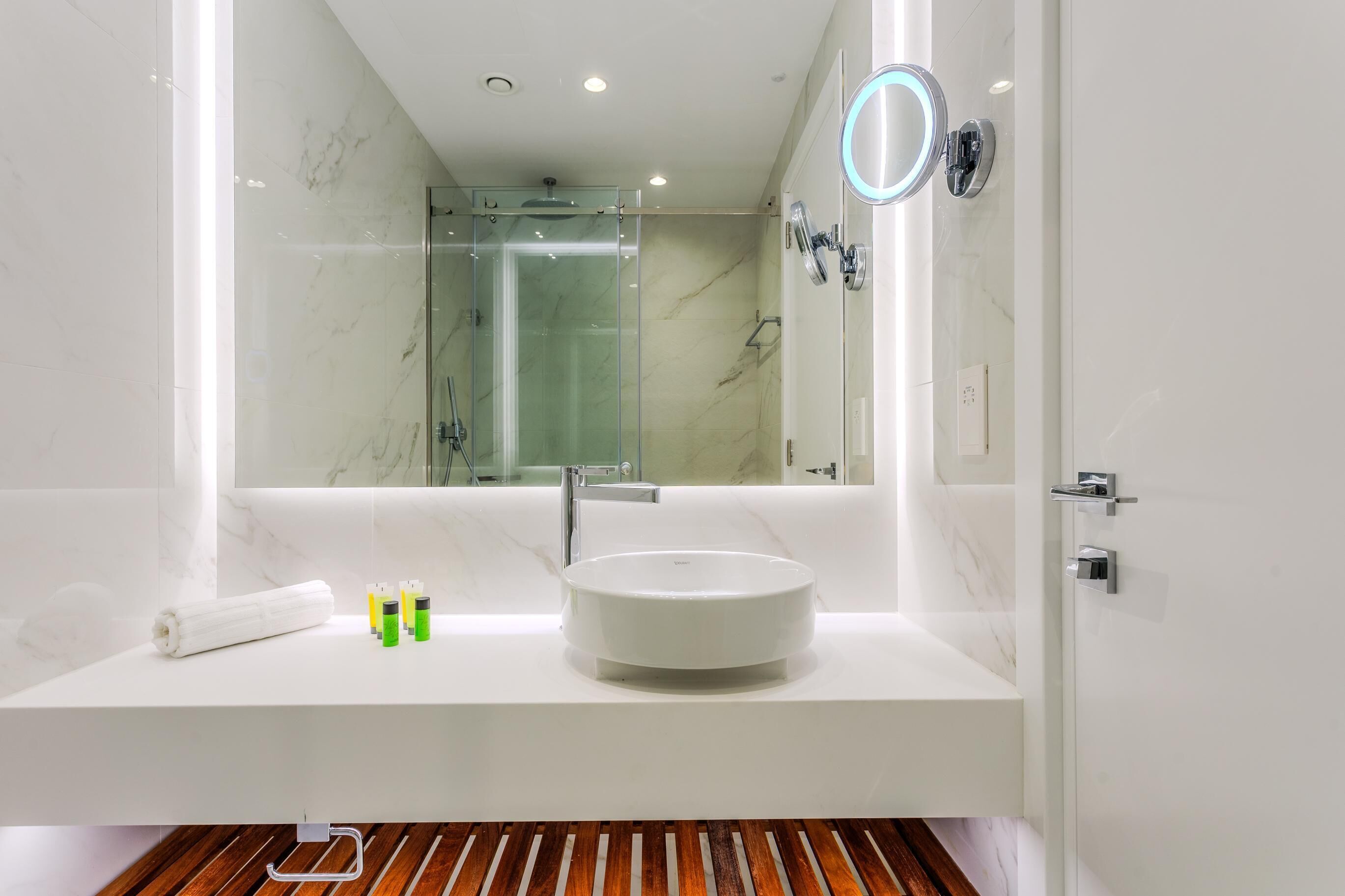 Un baño moderno con un espejo grande, un lavamanos redondo y una ducha con paredes de vidrio.