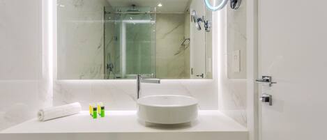 Un baño moderno con un espejo grande, un lavamanos redondo y una ducha con paredes de vidrio.