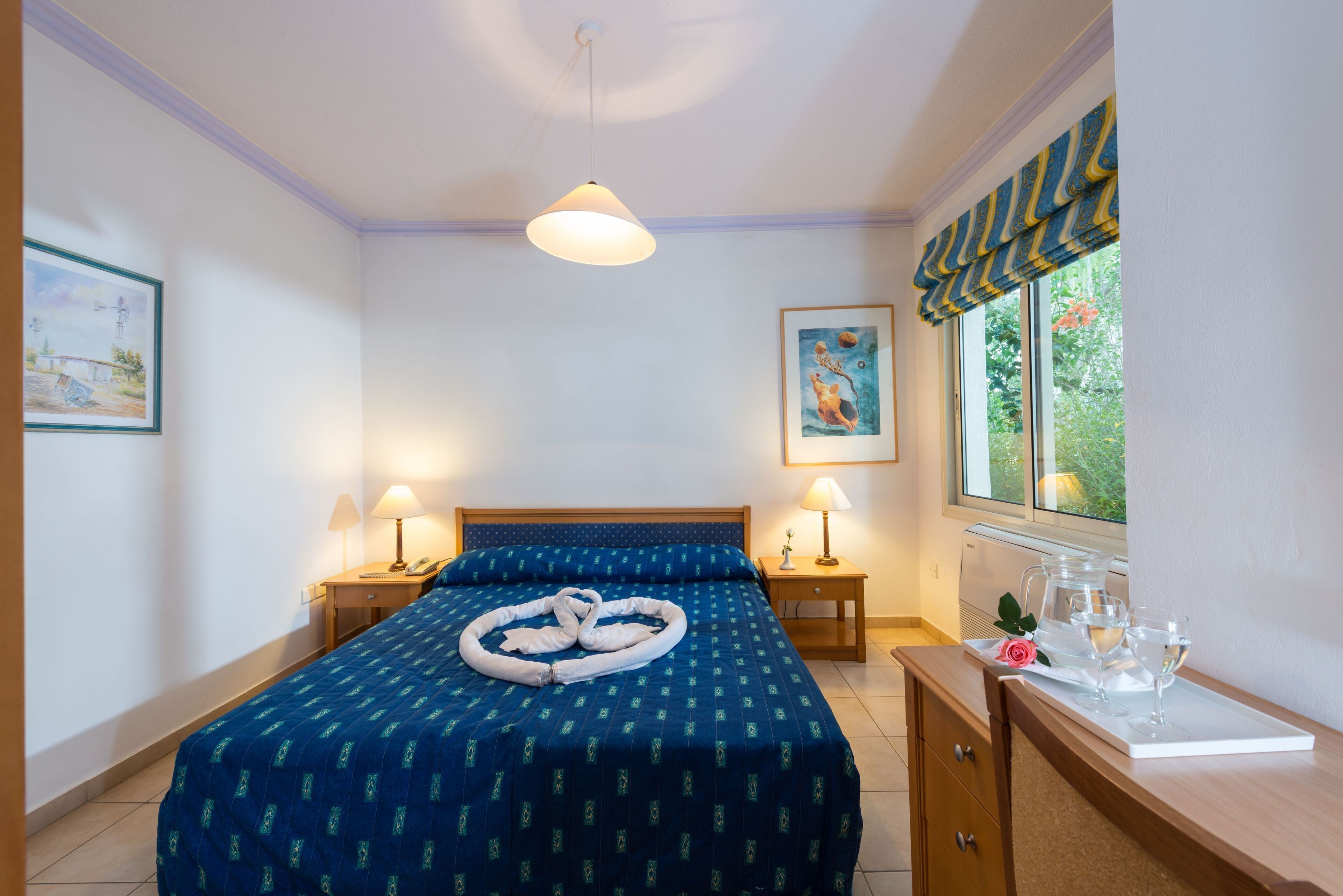 A neatly arranged bedroom with a bed, bedside tables, a desk, and a window with curtains.