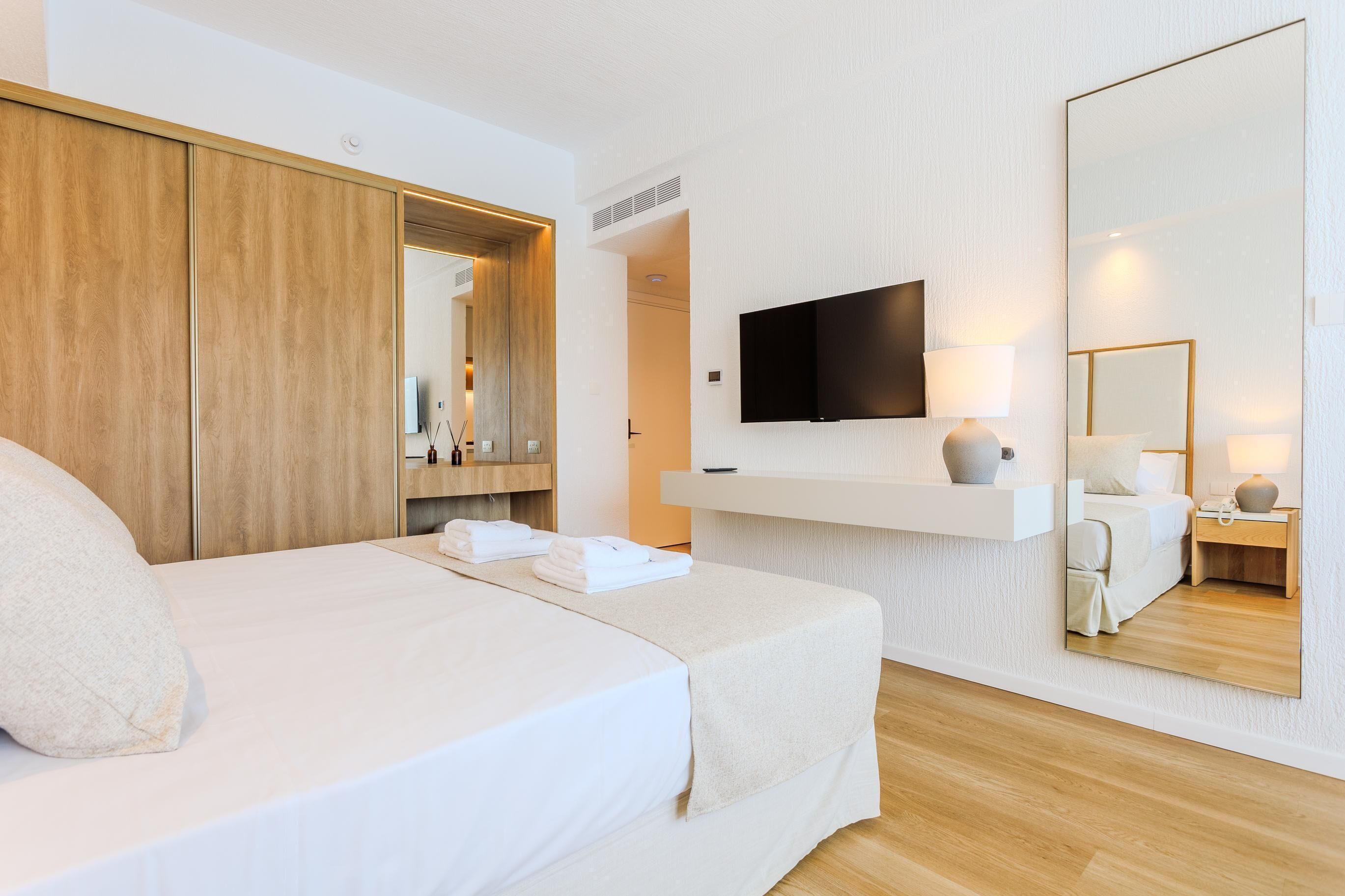 Ein Hotelzimmer mit Bett, Wandfernseher, Spiegel und Ablage mit Lampe.