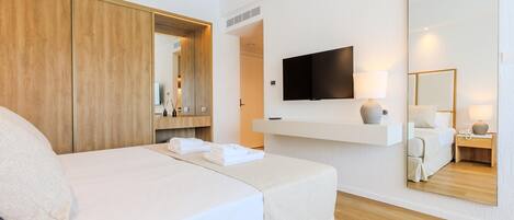 Ein Hotelzimmer mit Bett, Wandfernseher, Spiegel und Ablage mit Lampe.