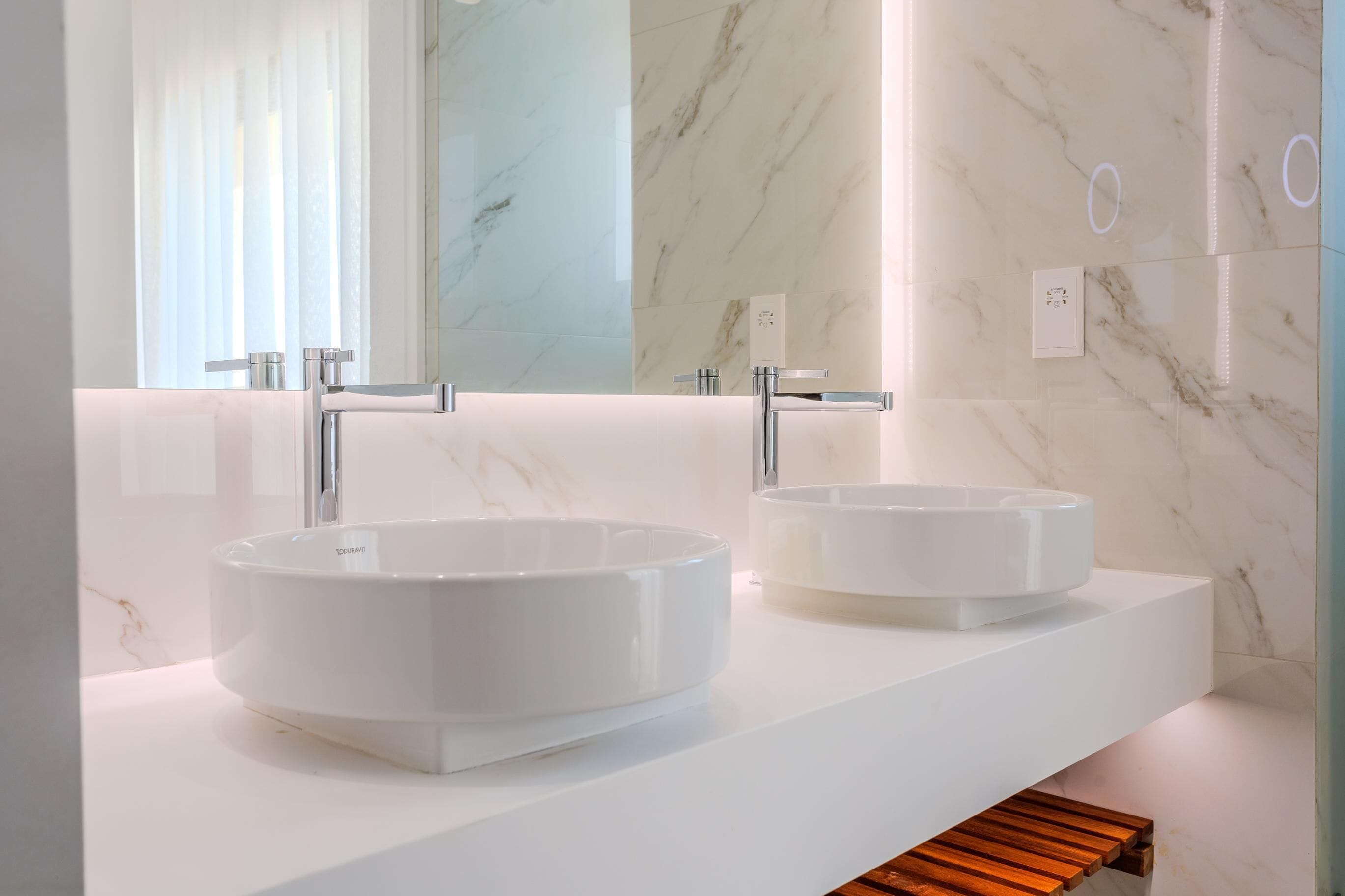 A modern bathroom with two white vessel sinks, a large mirror, and marble walls.
