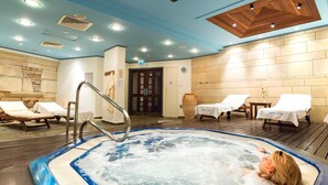 Un jacuzzi con una persona relajándose, rodeado de sillones de descanso y un techo de madera.