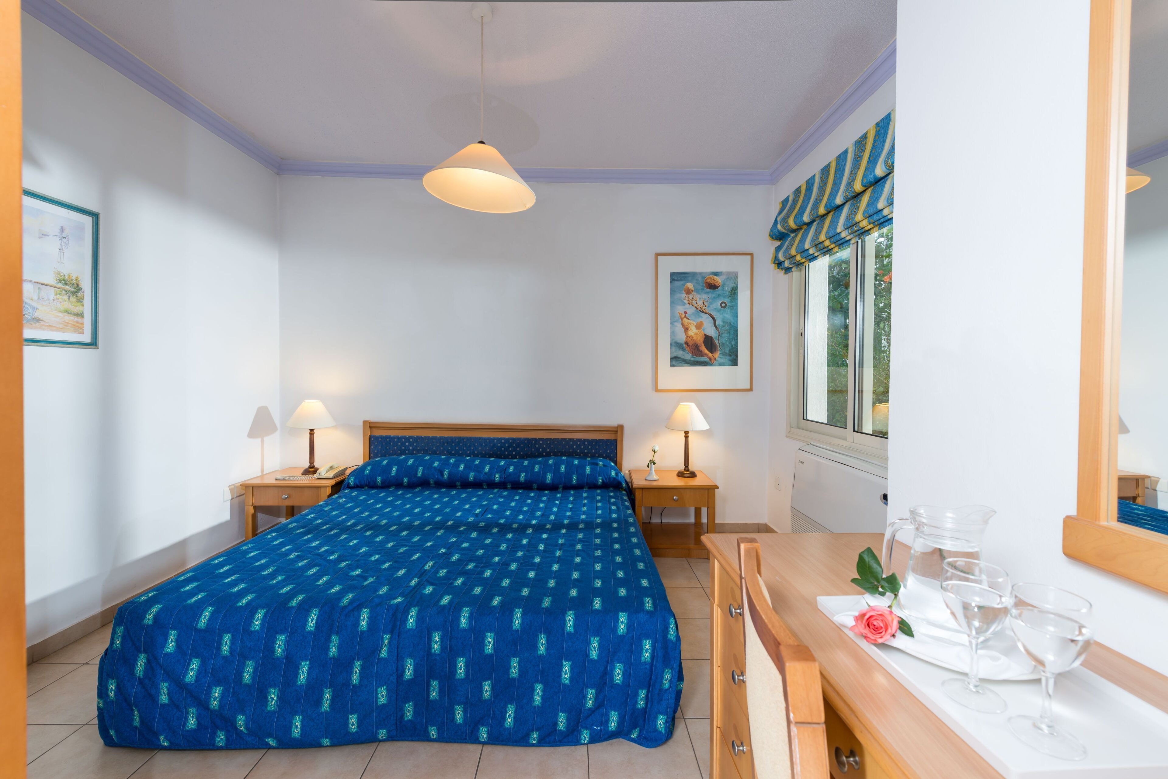 A bedroom with a bed, bedside lamps, a dresser, a mirror, and a window with curtains.