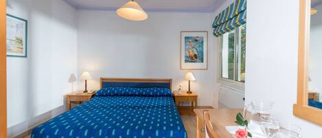 A bedroom with a bed, bedside lamps, a dresser, a mirror, and a window with curtains.