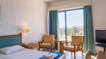 Une chambre d’hôtel avec un lit, deux chaises, une petite table, un téléviseur et un balcon avec des rideaux.