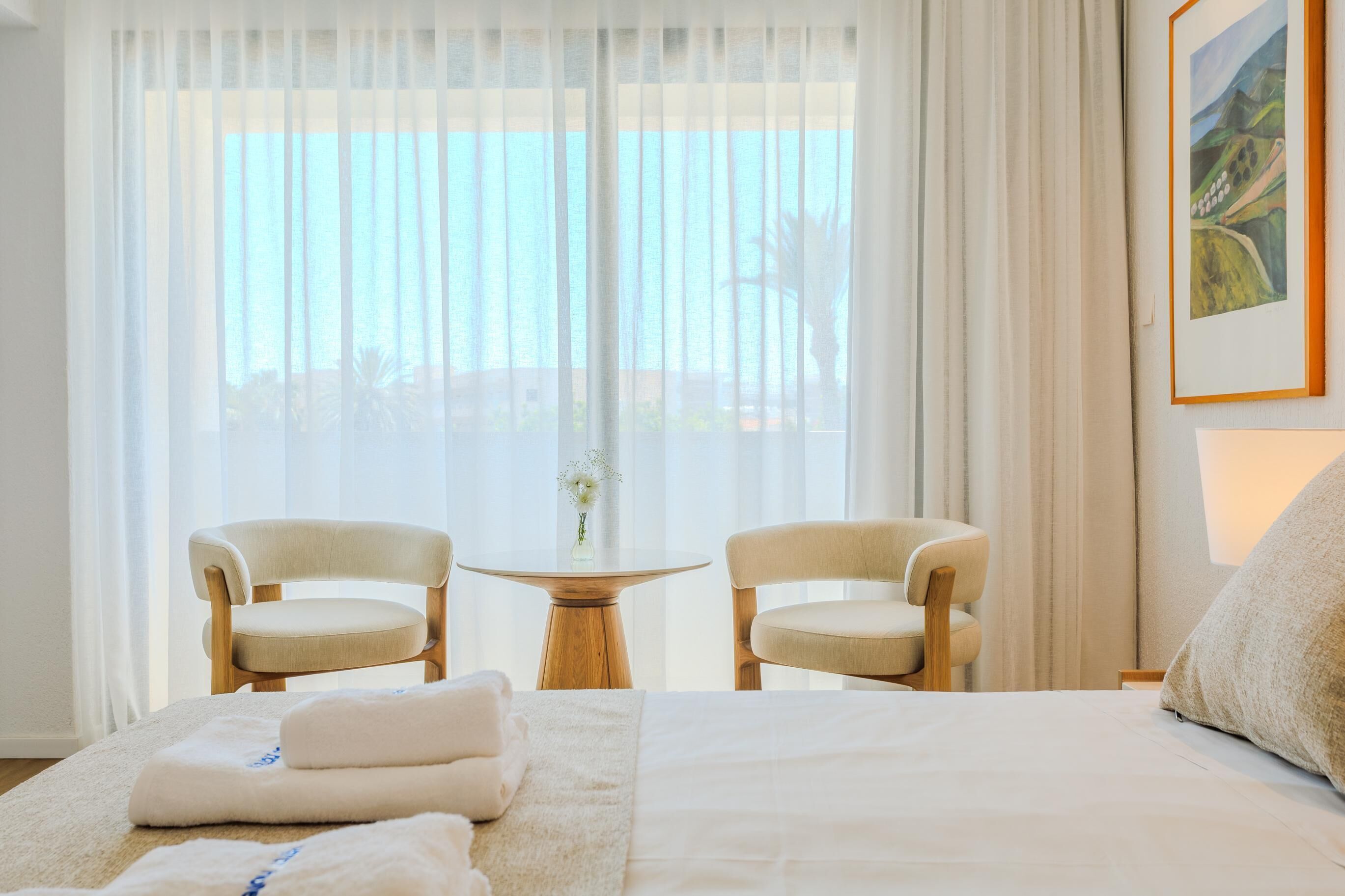Habitación de hotel con una cama, dos sillas, una mesita y un cuadro en la pared.