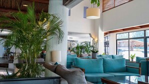 Un vestíbulo espacioso con sofás color turquesa, ventanas amplias y plantas de interior.