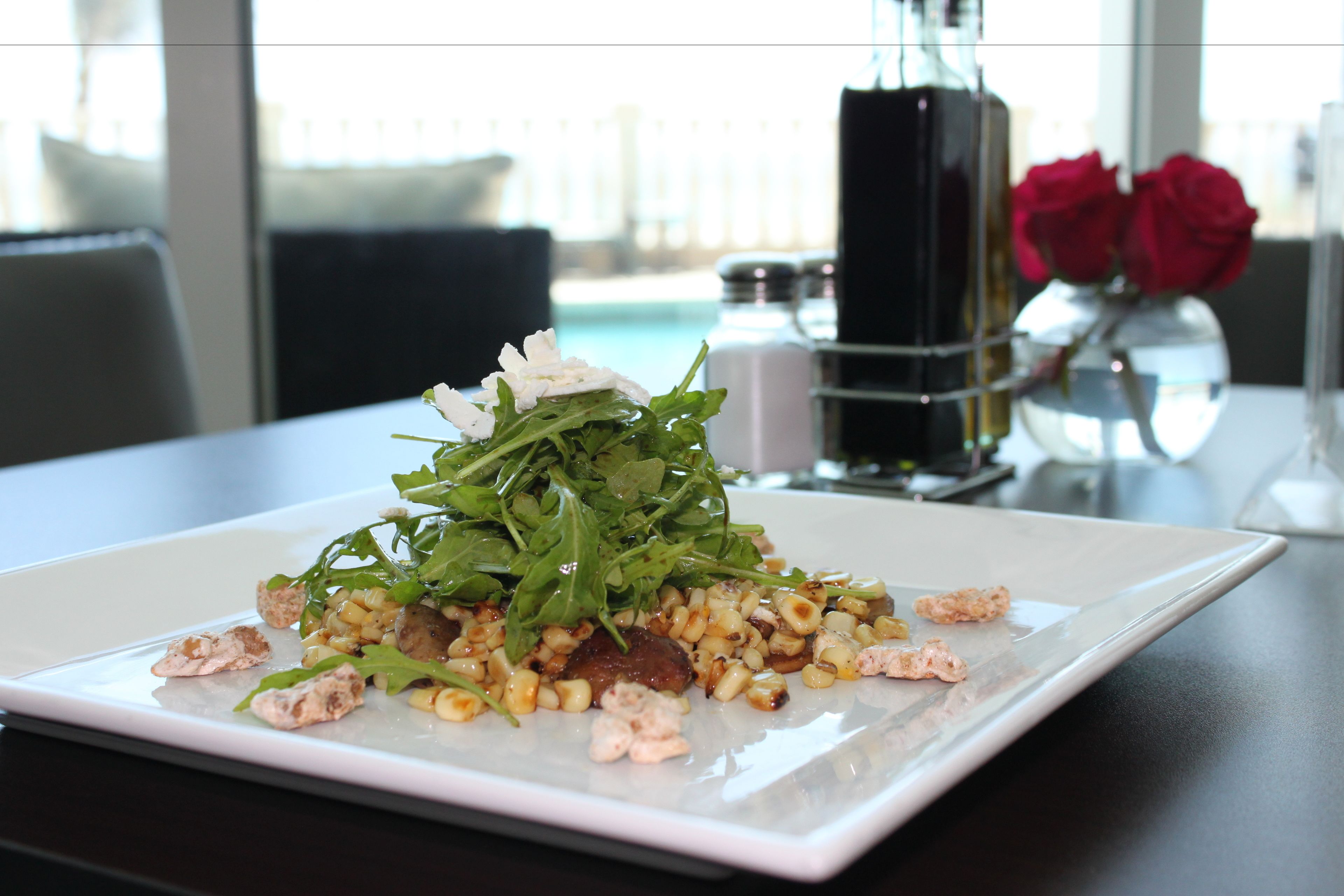 Une assiette rectangulaire blanche avec une salade, posée sur une table.
