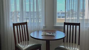 Un comedor con una mesa redonda y dos sillas de madera, una revista sobre la mesa, y vista al mar a través de cortinas translúcidas.