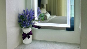 Casa de banho com bancada de mármore, um vaso branco com flores roxas e um espelho com moldura iluminada.