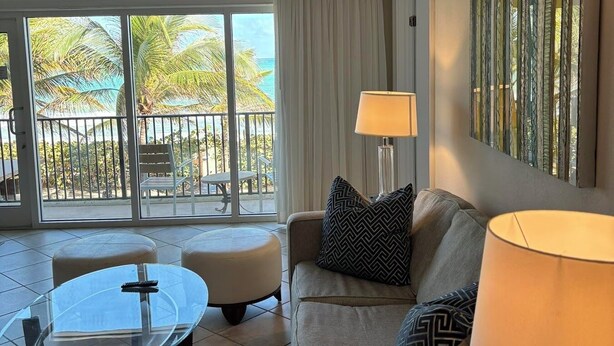 A living room with a glass table, a sofa, two lamps, and a view of the ocean through large windows. - The Sea Lord (Lauderdale-by-the-Sea)