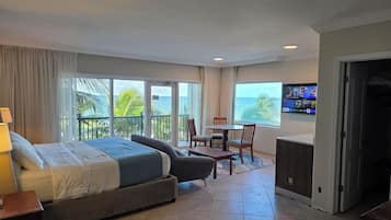 A hotel room with a bed, a desk, a chair, a TV, and a balcony with a view of the ocean.