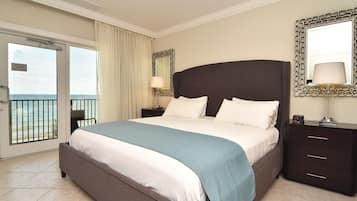 Habitación de hotel con una cama grande, una mesita de noche, un espejo y vista al océano a través de una puerta corrediza.