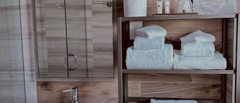 A modern bathroom with a wooden wall, a large mirror, a white sink, and neatly folded towels on shelves.