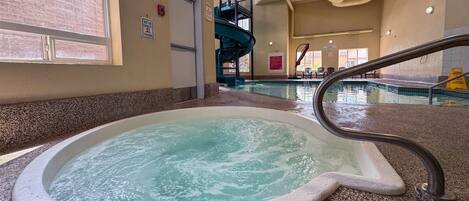 Un espace avec un jacuzzi, une piscine, un toboggan et une rampe d’appui.