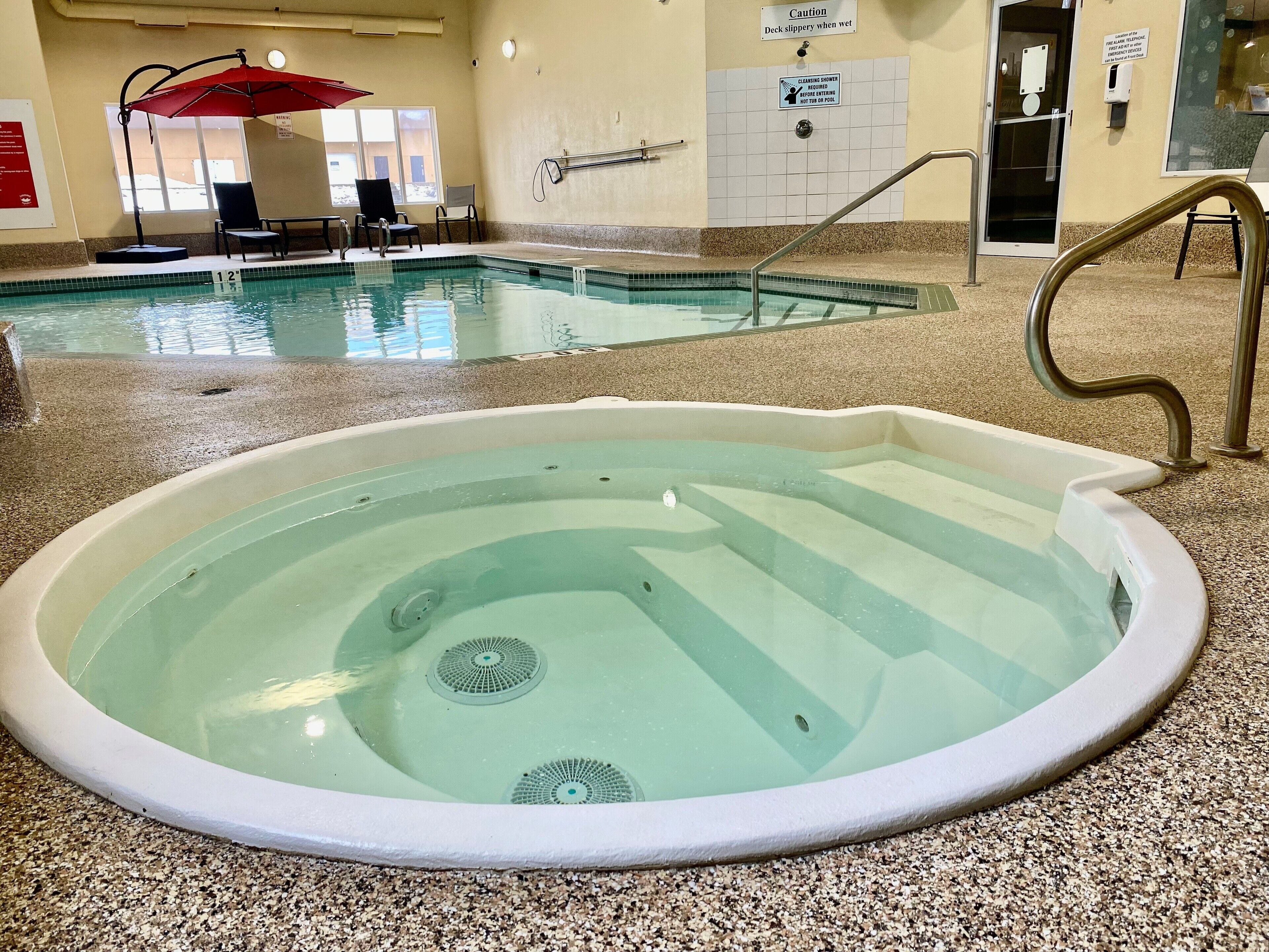 An indoor swimming pool with a hot tub, lounge chairs, and safety signage.