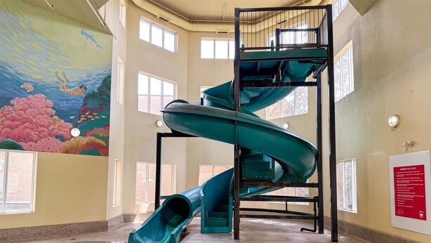 Una piscina interior con un tobogán en espiral, un mural de una escena submarina y una zona de piscina con un cartel de seguridad.