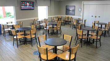 A conference room with multiple tables and chairs, a large screen on the wall, and a framed picture.