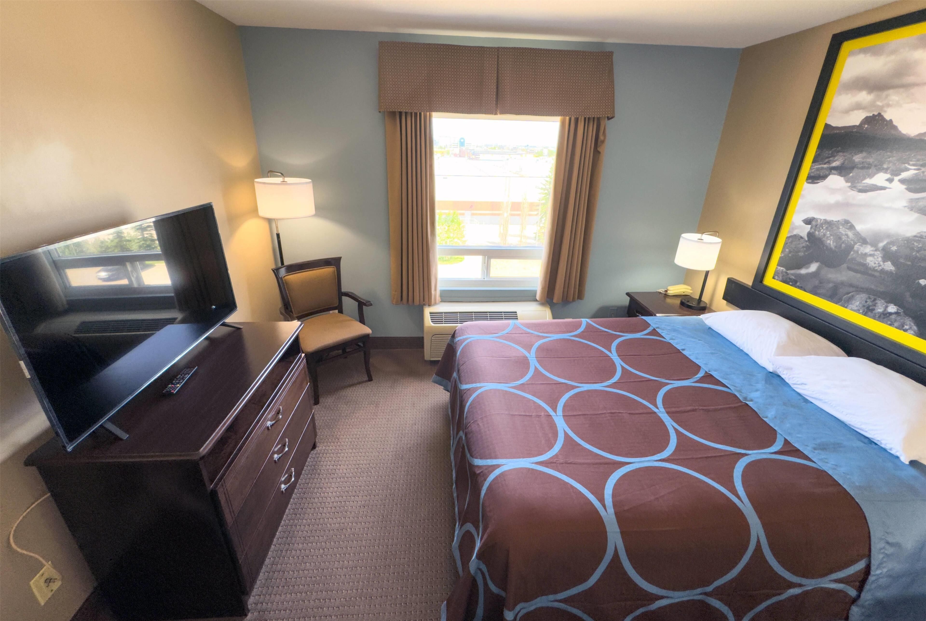 A hotel room with a bed, a desk with a computer, a chair, a lamp, and a window with curtains.