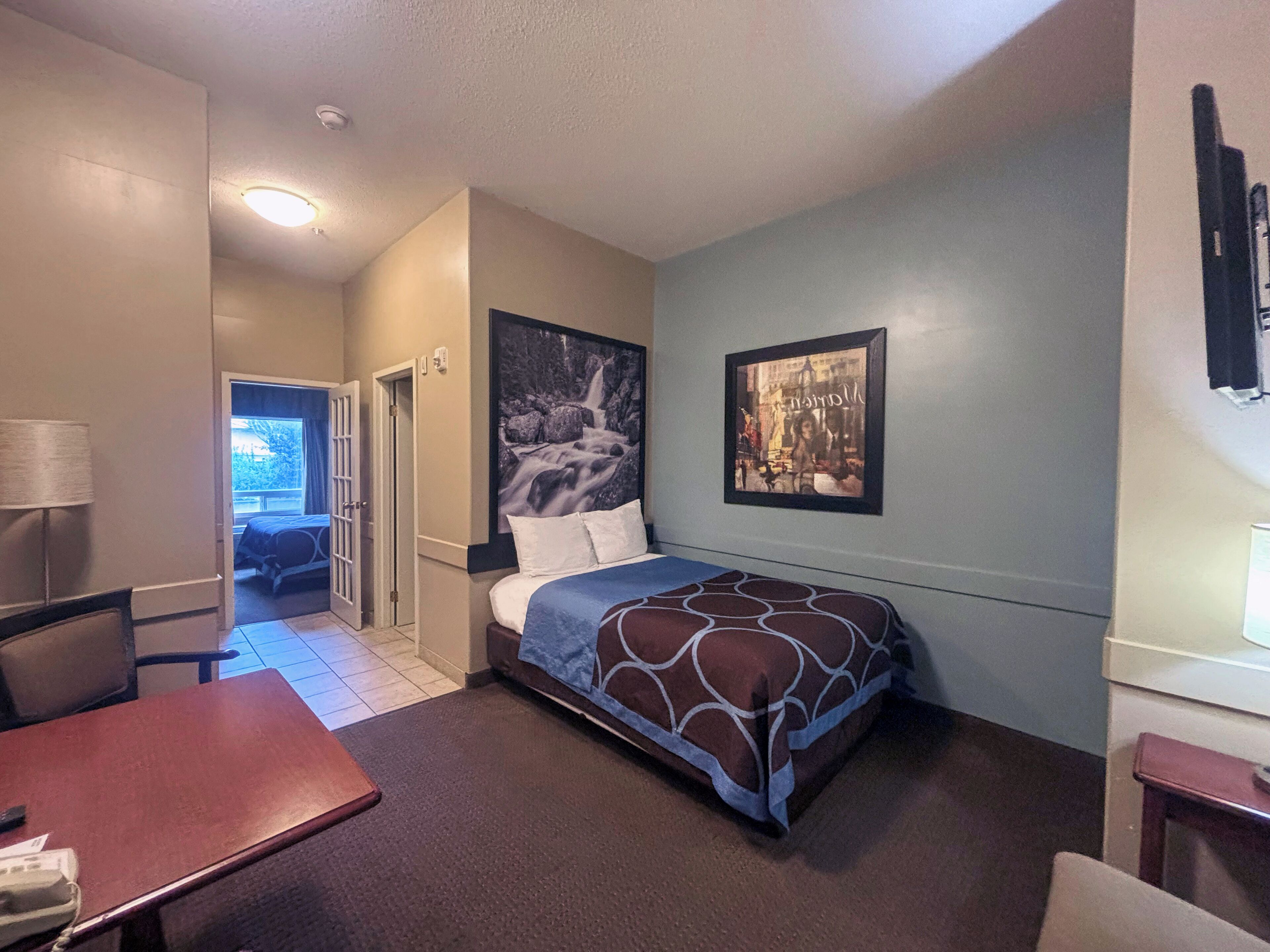 Een hotelkamer met een bed, een bureau, een stoel, een deur naar een balkon en een groot raam.