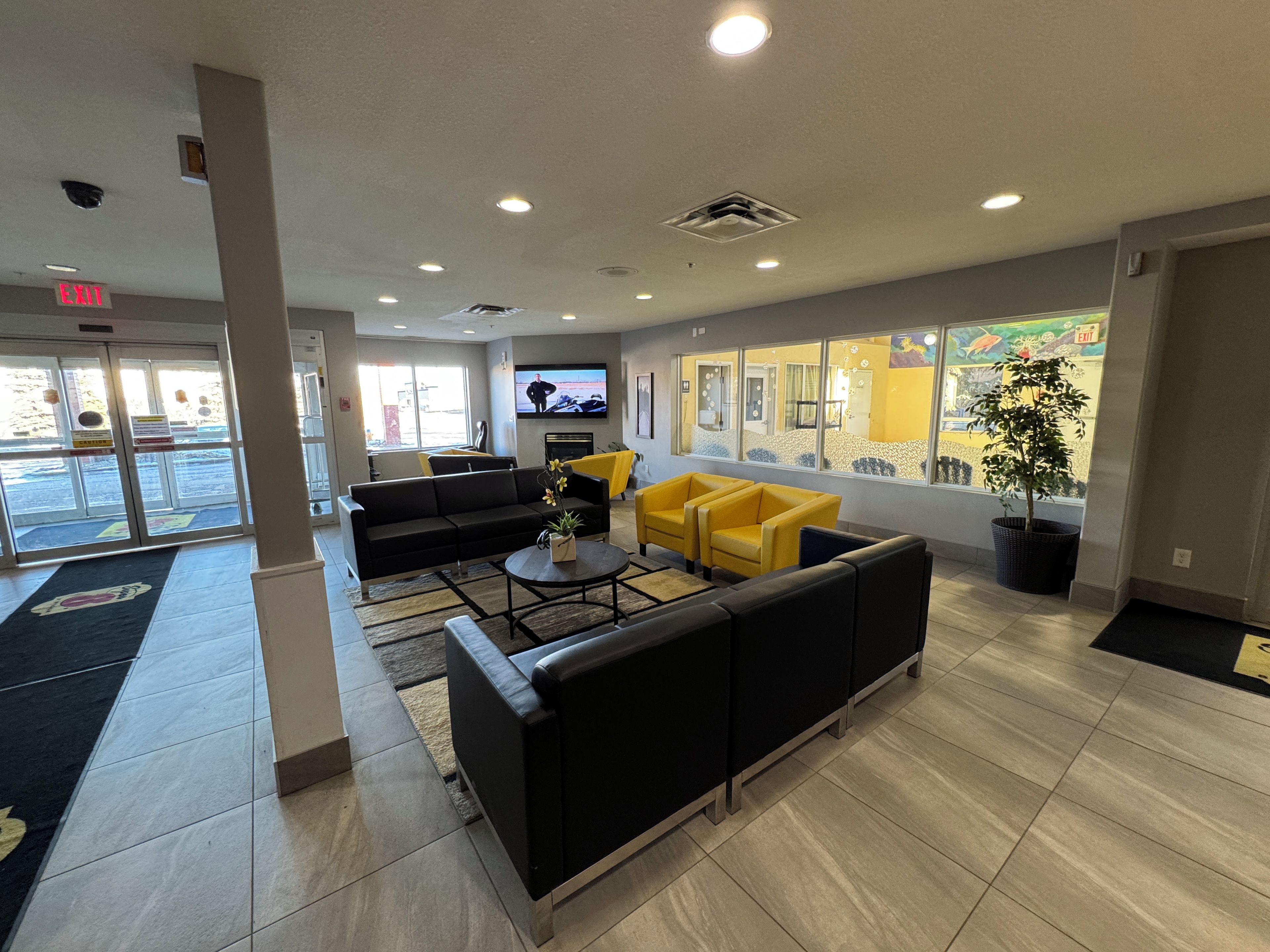 A lobby with a black sofa, yellow armchairs, a coffee table, and a TV screen.