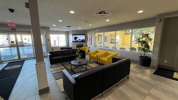 A lobby with a black sofa, yellow armchairs, a coffee table, and a TV screen.